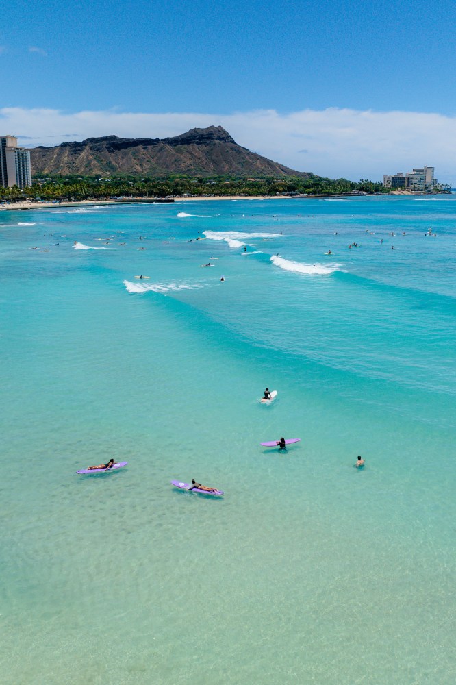 Surfers in turquoise ocean with a mountain and city skyline in the background.
