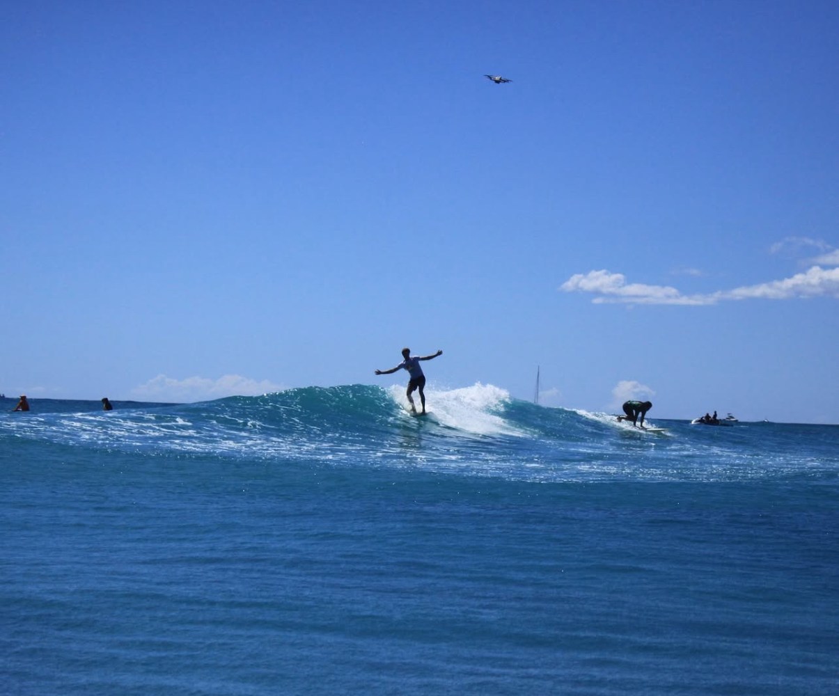 Surfer balancing on a wave with clear blue sky and sea.