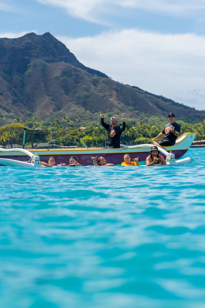 People in a canoe on clear blue water with mountains in the background.