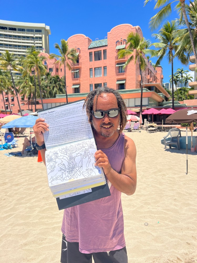Man in sunglasses holds open book on a sunny beach with pink hotel and palm trees in background.