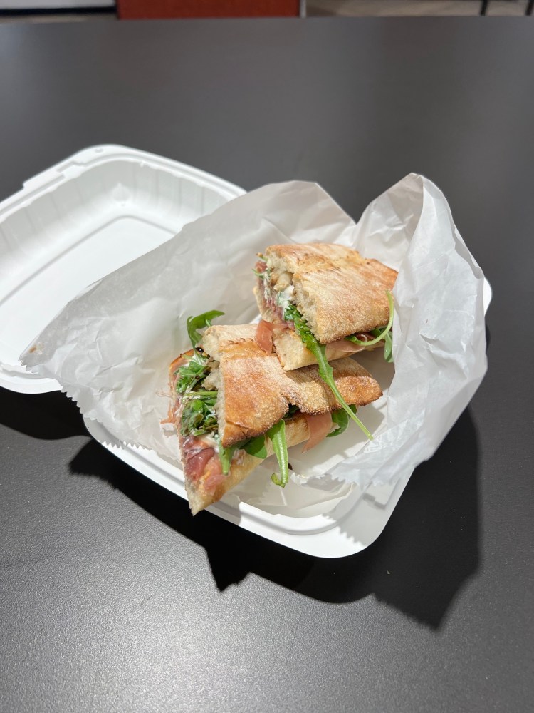 Sandwich halves with greens in a white takeout container on a dark table.