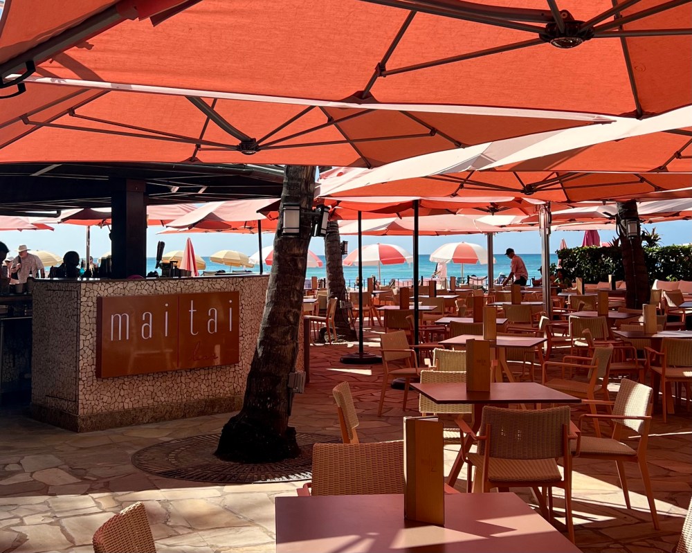Outdoor restaurant with orange umbrellas, tables, chairs, and ocean view.