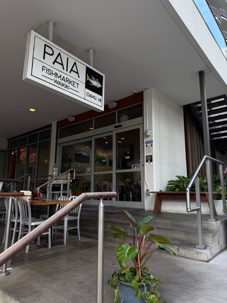 Entrance to Paia Fish Market Waikiki with tables and chairs outside.