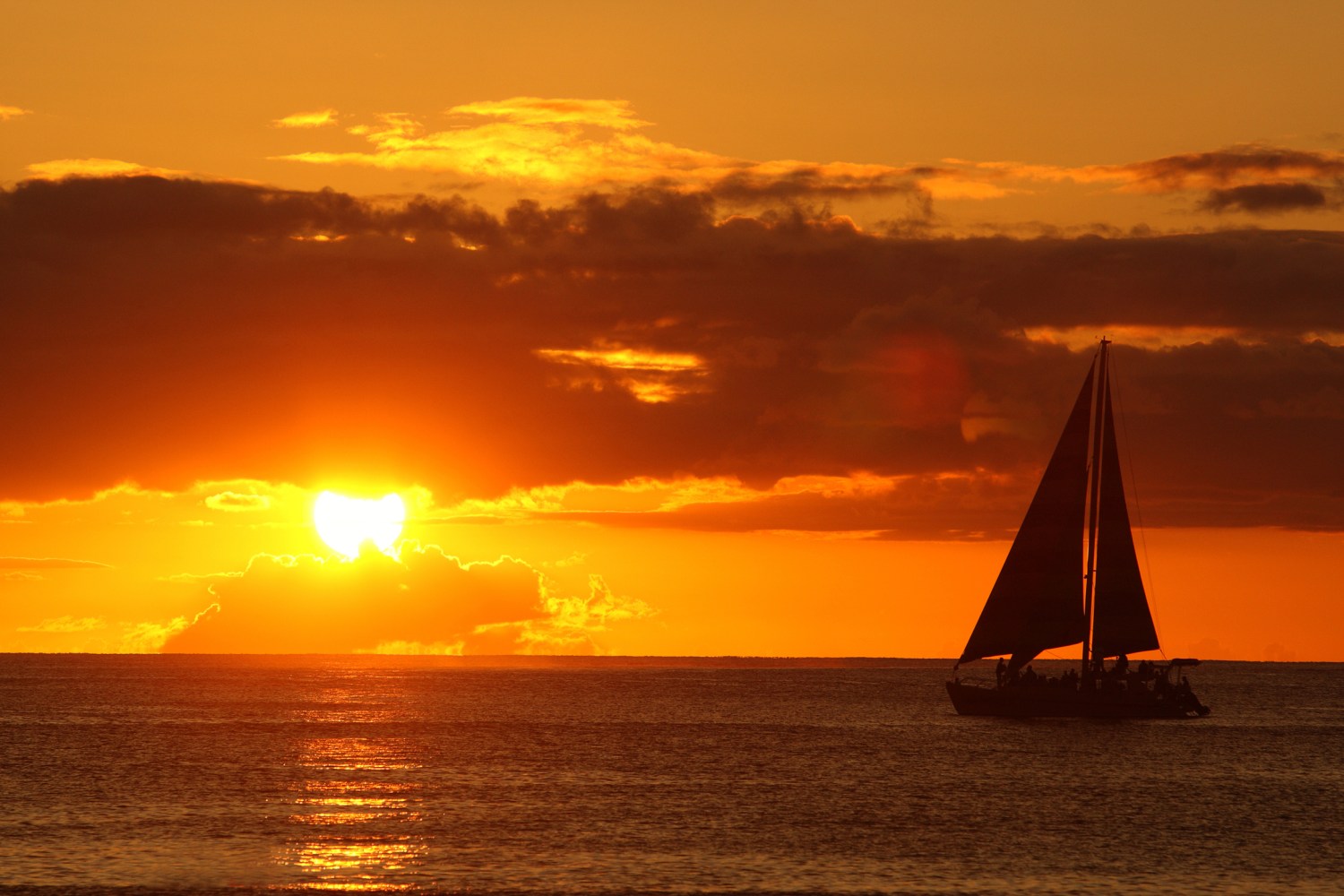 Silhouetted sailboat on ocean at sunset with vibrant orange sky.