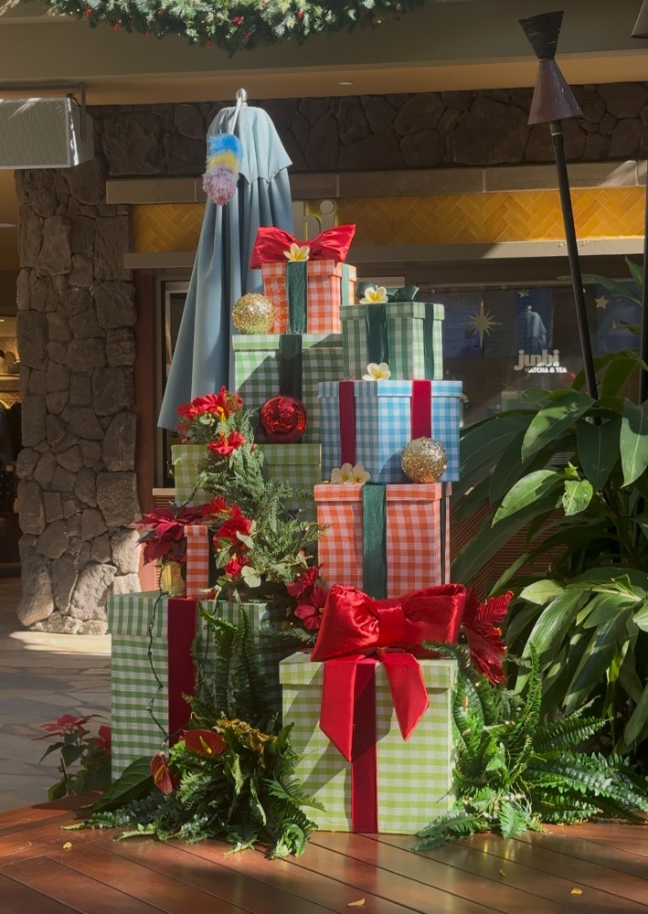 Stack of colorful gift boxes with ribbons, surrounded by festive greenery and ornaments under a wreath.