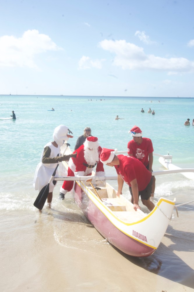 People in Santa costumes moving a canoe on a beach.