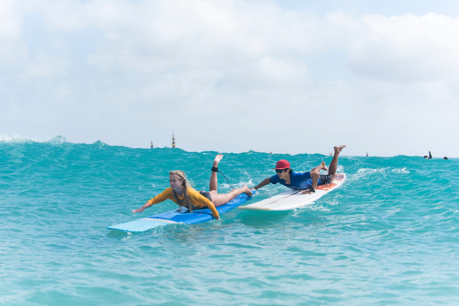 Two people paddle on surfboards in the ocean under a cloudy sky.