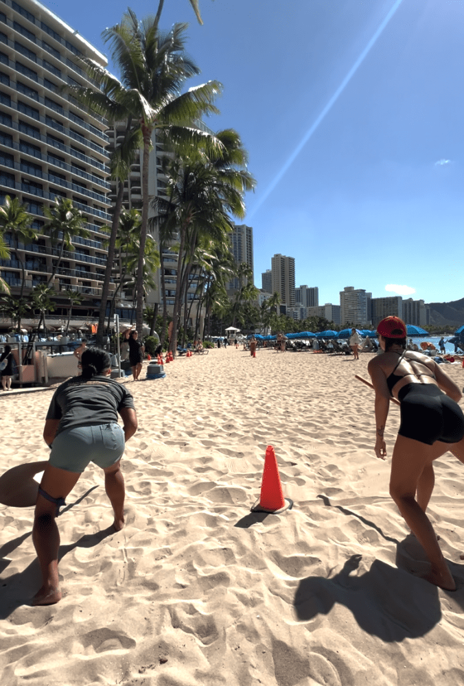 Two people exercising on a sunny beach near city buildings and palm trees.