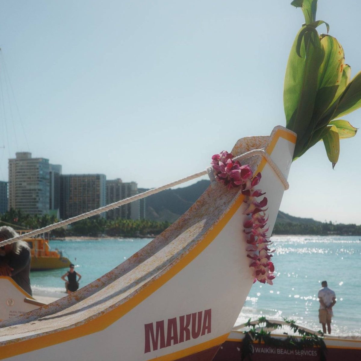 Close-up of a boat named 'Makua' adorned with flowers on a sandy beach.
