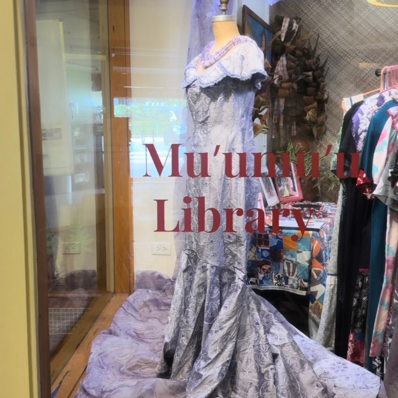 Elegant lavender dress on display in a glass window with fabric draped around it.