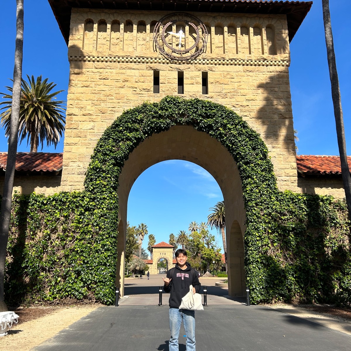 Person standing in front of ivy-covered arch at a historic stone building.