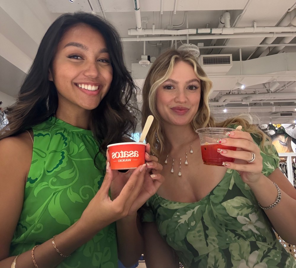 Two women smiling indoors holding desserts, one with ice cream, the other with a fruit cup.