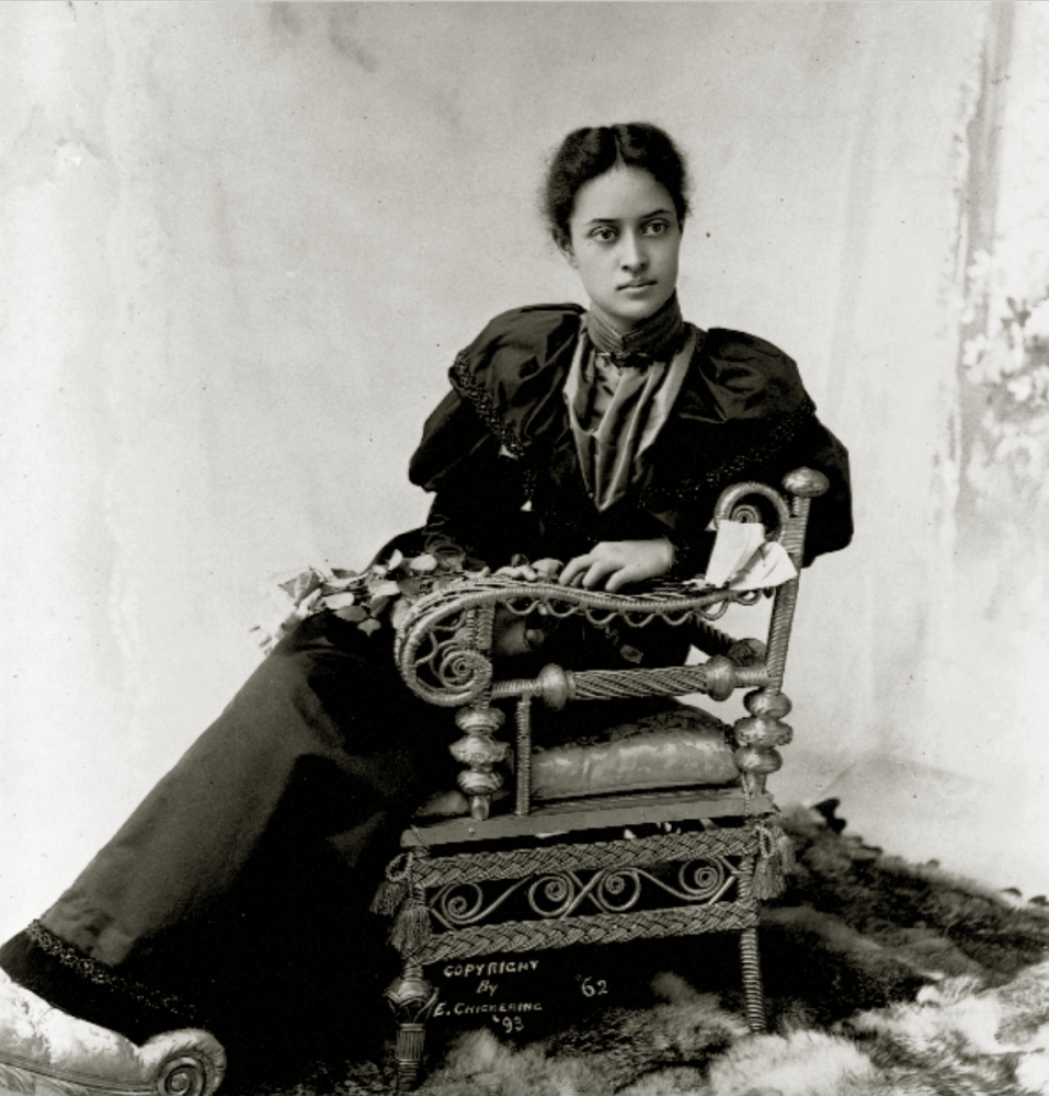 Vintage photo of woman in formal attire sitting on an ornate chair.