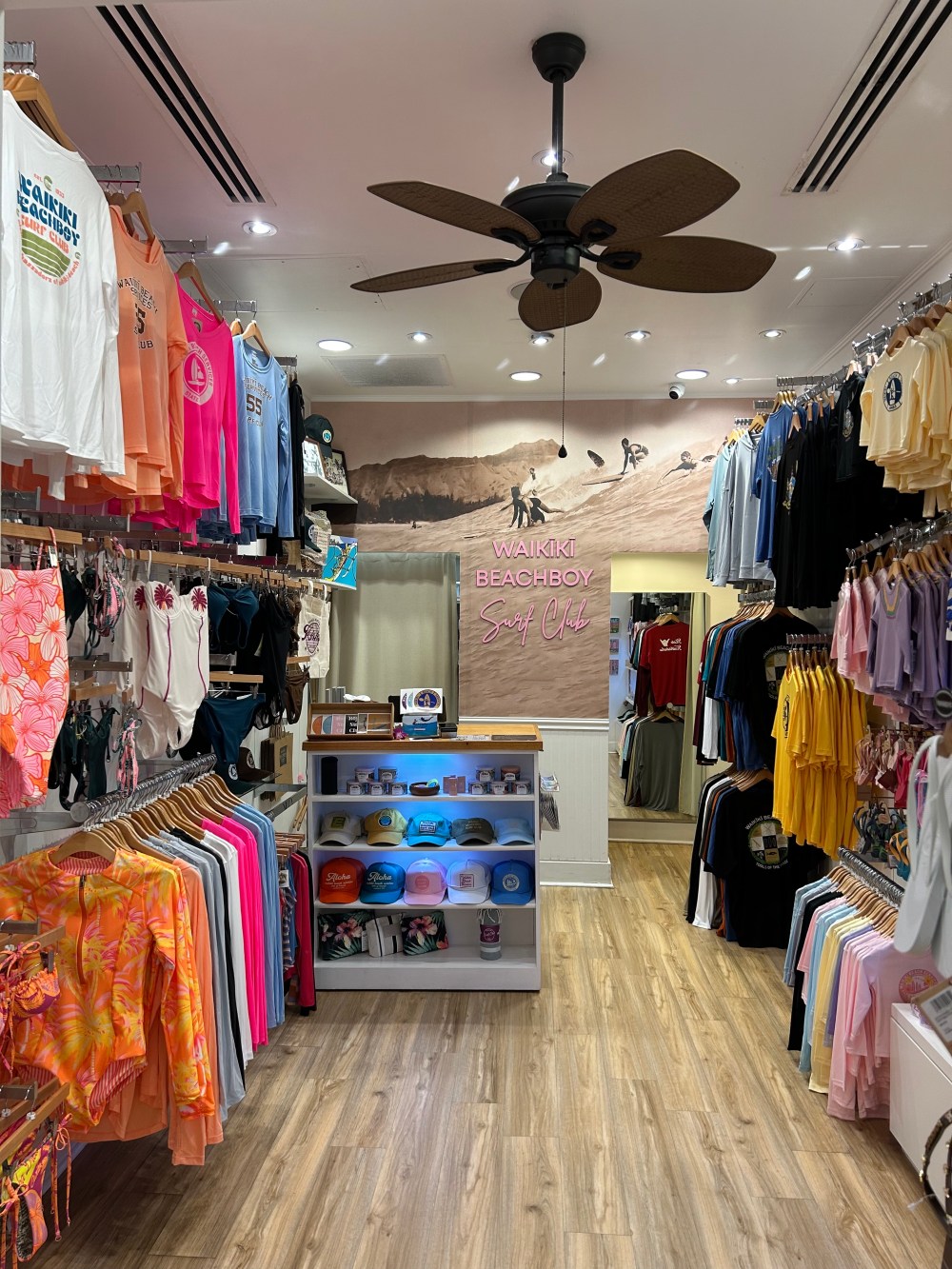 Clothing store interior with colorful shirts and hats, wooden floor, surf-themed decor.