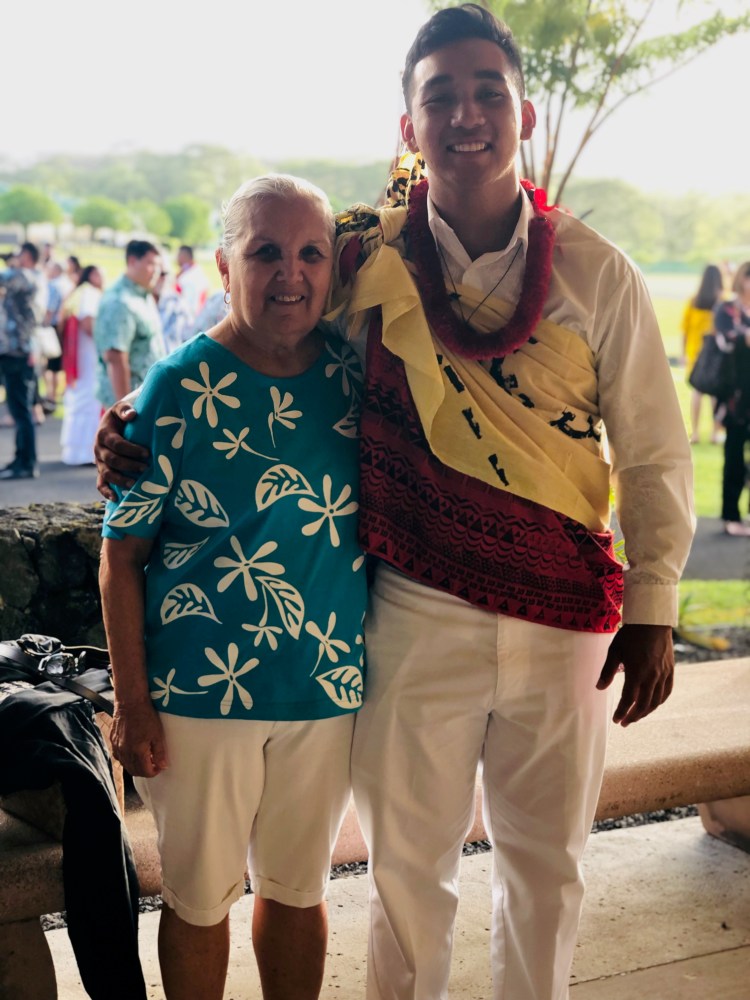 Older woman and young man in traditional attire smiling outdoors.