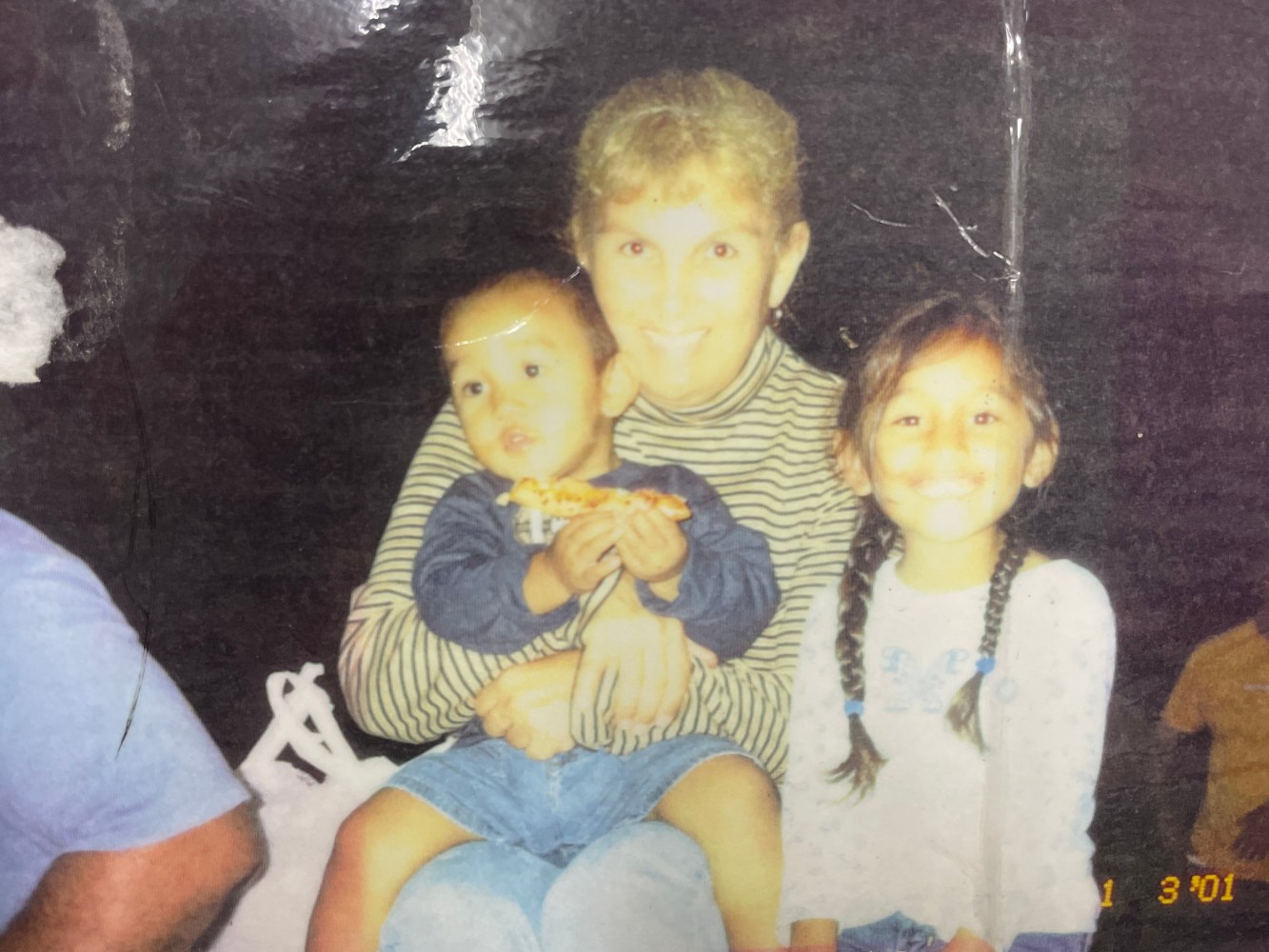 A woman with short hair holds a baby and sits next to a smiling girl with braids.