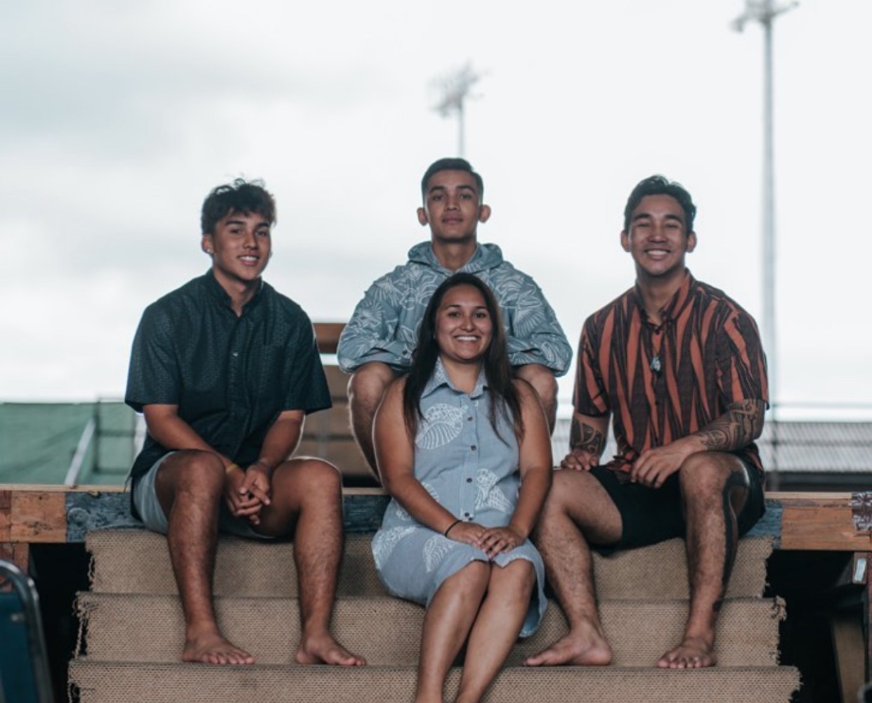 Four people sitting on steps, three men and one woman, smiling at the camera.