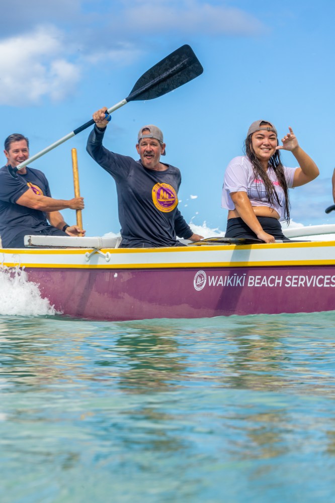 Three people paddling a purple canoe on clear water.