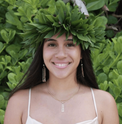 Person smiling with leafy headdress, green foliage background.