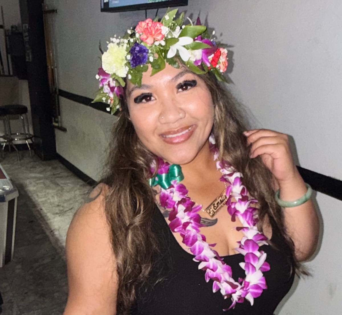 Person wearing a floral crown and lei, smiling indoors.
