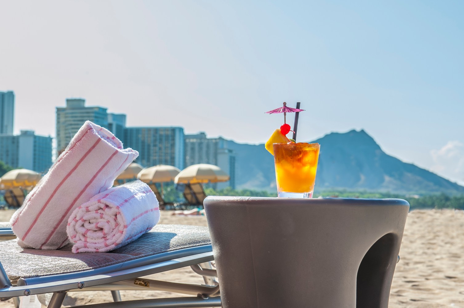 Beach scene with cocktail, towels on chair, city skyline and mountain in background.