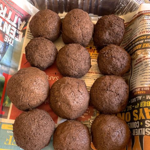 Twelve round chocolate cookies on newspaper background.