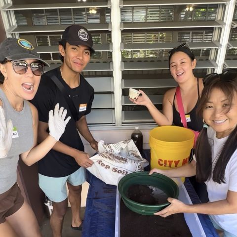 Four people smiling, working with soil and planting materials indoors.