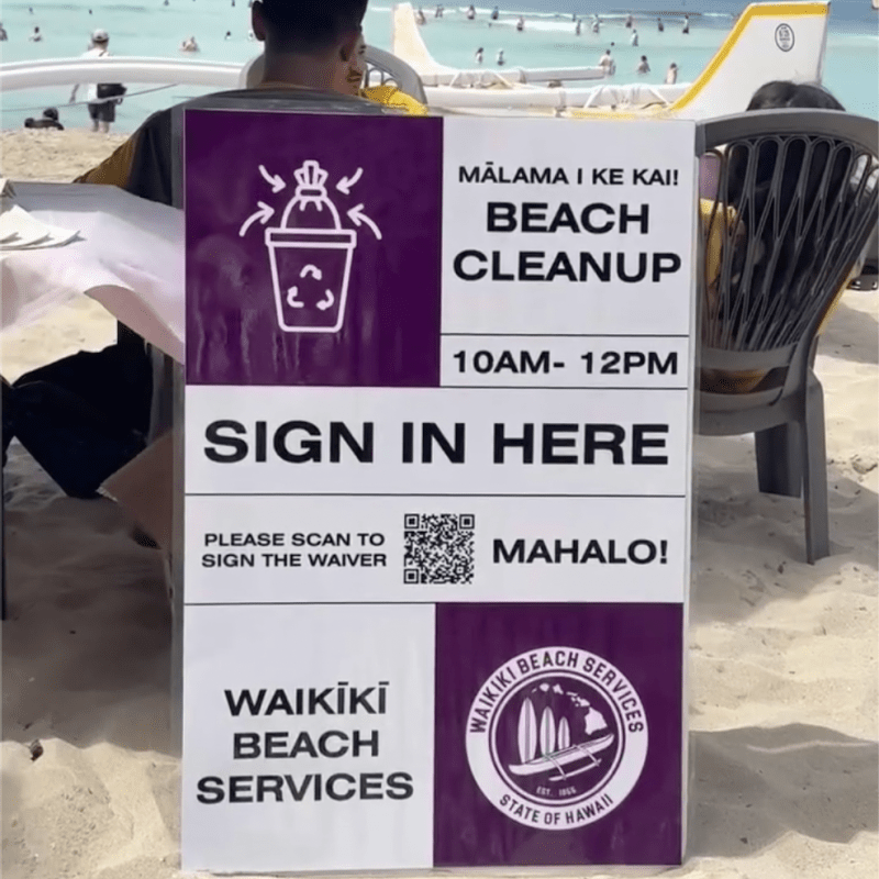 Beach cleanup sign with text and icons in front of a sandy beach.