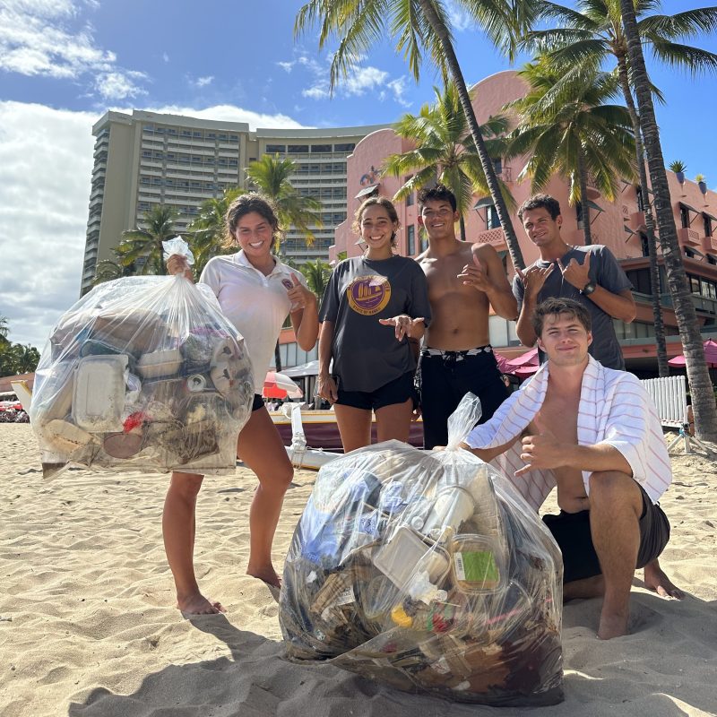 Group on beach with trash bags filled with litter, palm trees in background.