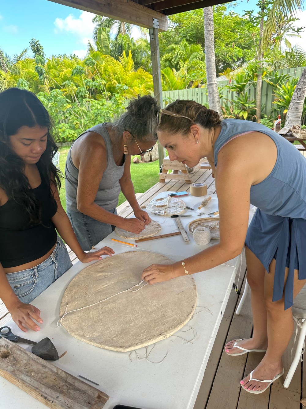 Three women working on a craft project at an outdoor table.