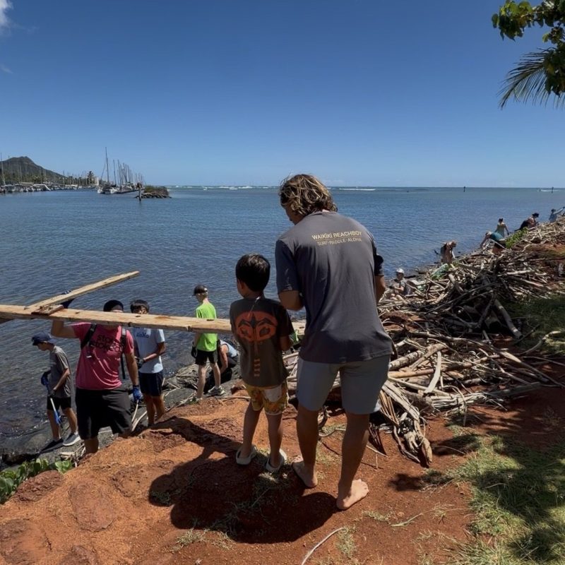 People cleaning up debris by the shore under a clear blue sky.